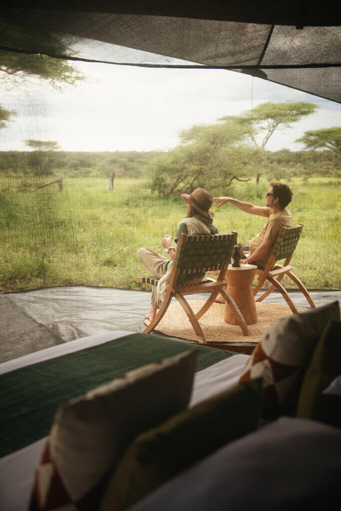 Ein Paar sitzt vor dem ihrem Zelt und blickt auf die Serengeti. 
