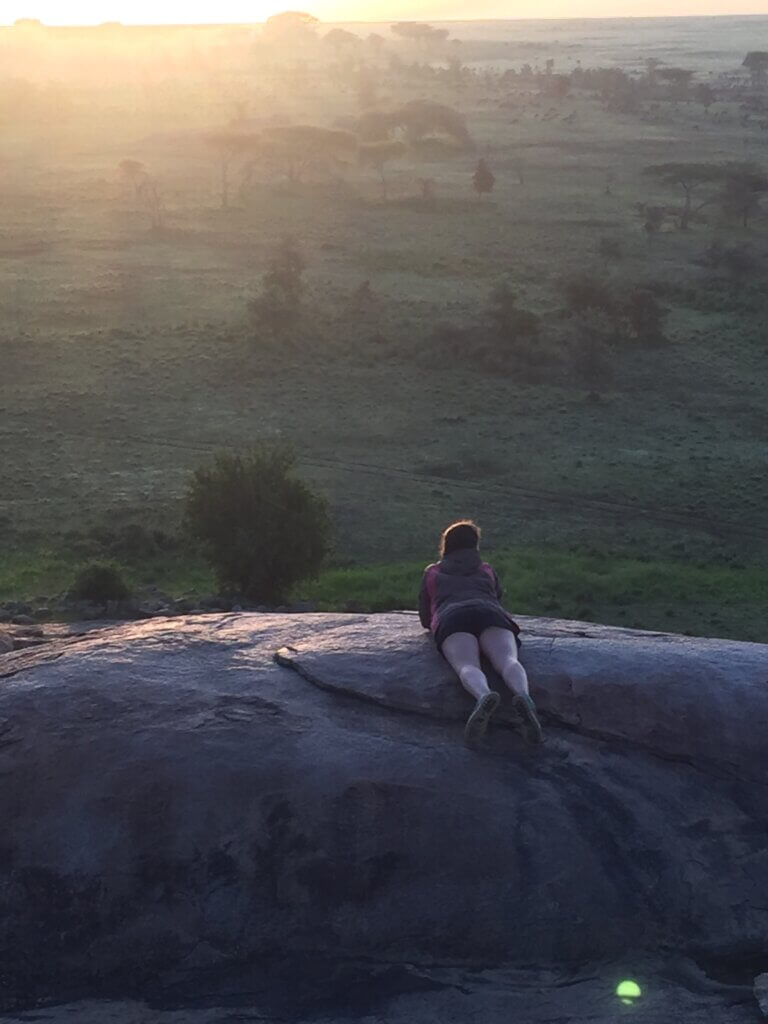 Eine Frau liegt auf einem Felsen und blickt im Sonnenuntergang auf die Serengeti. 