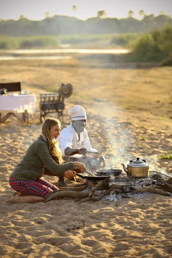 Gemeinsam mit einem Gast bereitet der Koch über dem offenen Feuer das Abendessen zu. 