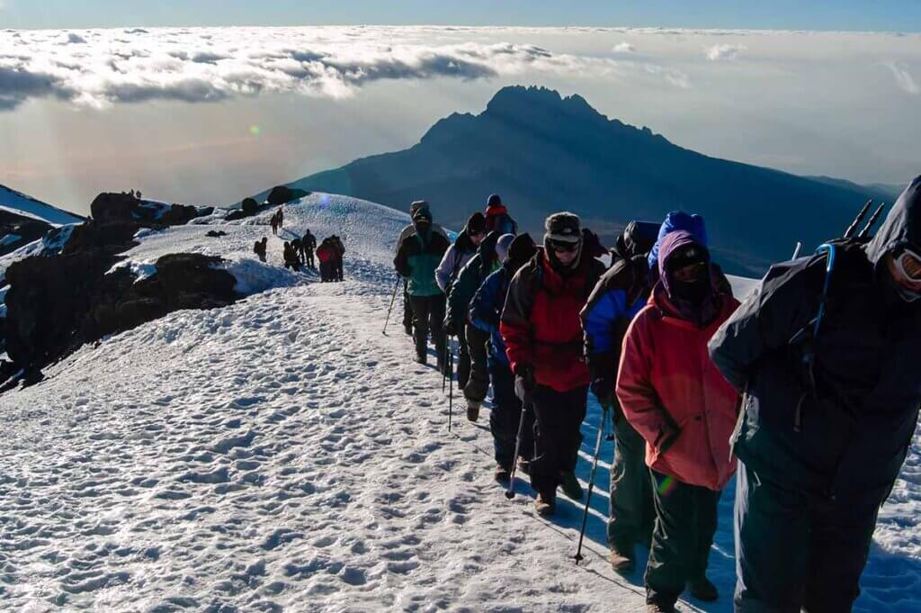 Ein große Gruppe Bergsteiger stellt sich an, um den Uhuru Peak am Kilimanjaro zu besteigen. Es hat geschneit. Die Aussicht auf den Mawenzi ist bestechend.