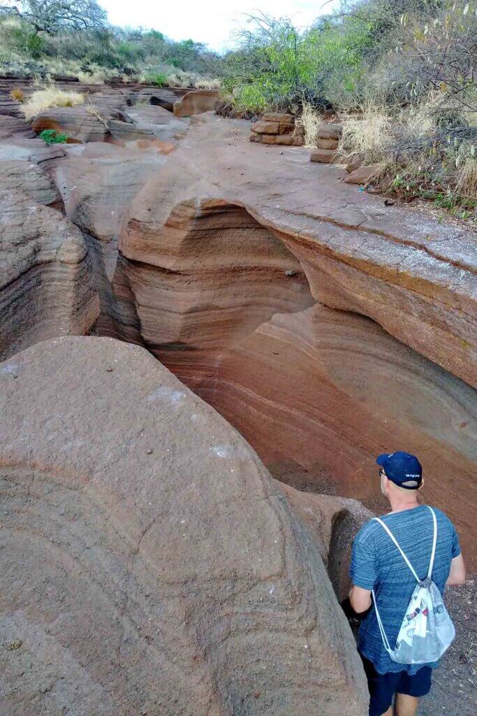 Ein Wanderer steht in einem Canyon, der durch unterschiedlich rötliche Gesteinsschichten charakterisiert ist.