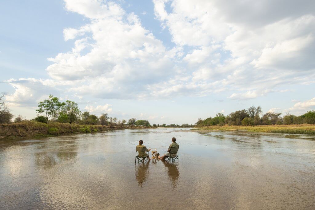 Zwei Personen sitzen im Mwaleshi River und blicken in die Weite. Wasser ist lebensnotwendig, umso mehr in Afrika. Verhalten wir uns so, dass wir möglichst wenig die Natur belasten. 