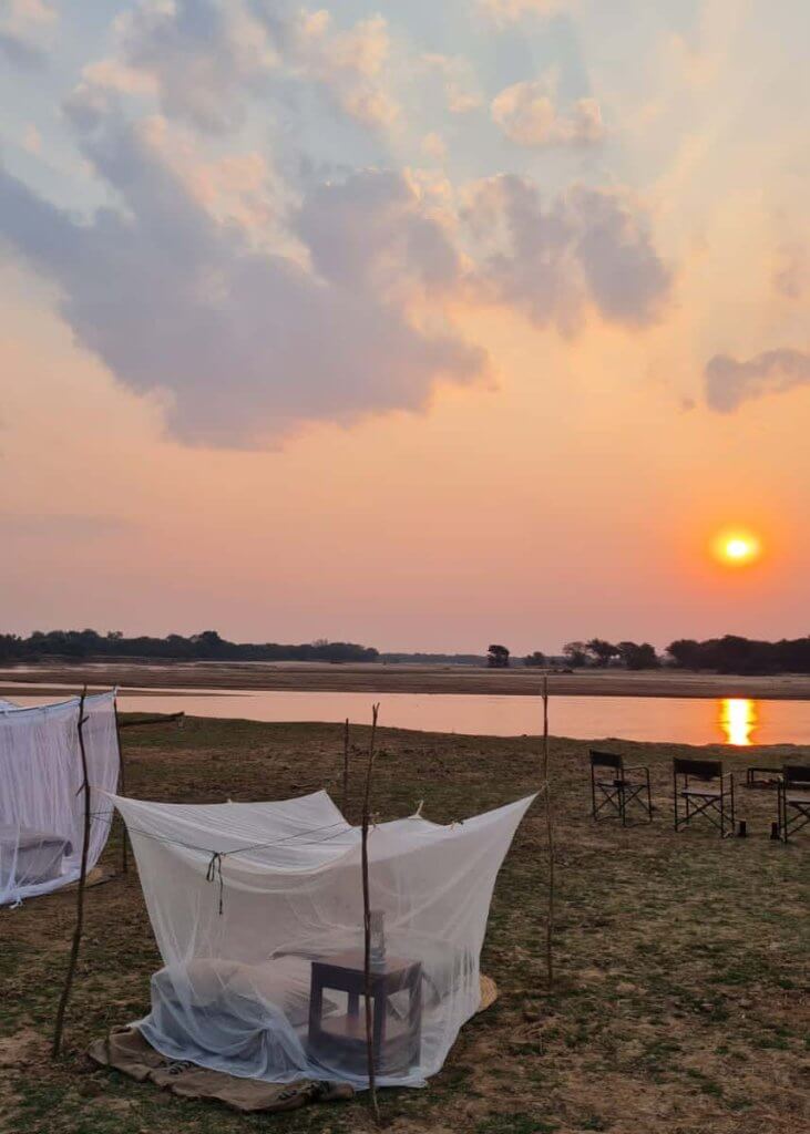 Die Sonne geht über dem Luangwa River unter und taucht das Fly Camp am Fluss in warme Farben. 