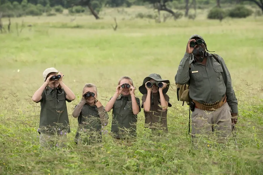 Afrikanische Guides haben Spaß daran, sich mit Kindern zu beschäftigen. Vier wissbegierige Kinder und der Guide versuchen mit den Ferngläsern, ein Tier in der Distanz zu spotten. 